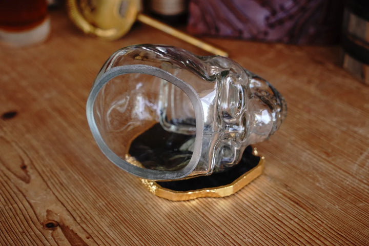 Clear skull-shaped whiskey glass, side view on coaster