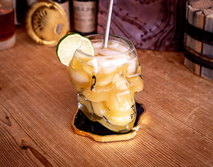 Skull whiskey glass with yellow drink, lime wedge, and metal straw