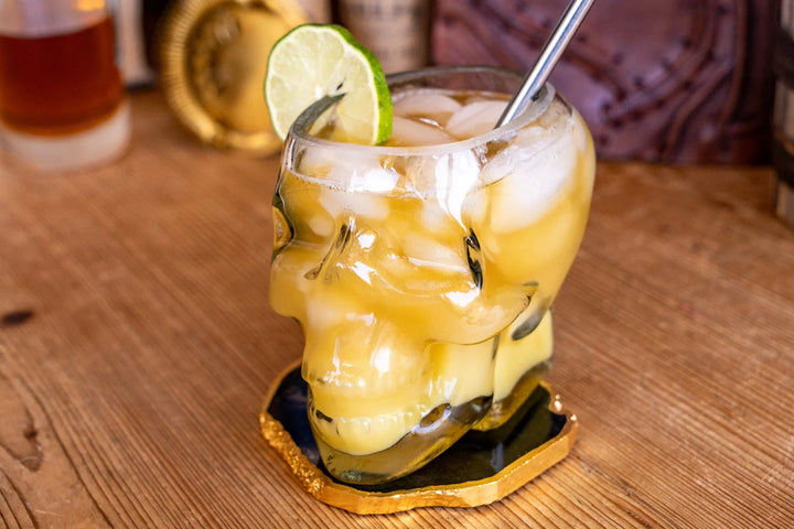 Skull whiskey glass with yellow drink, lime wedge, ice, and metal straw