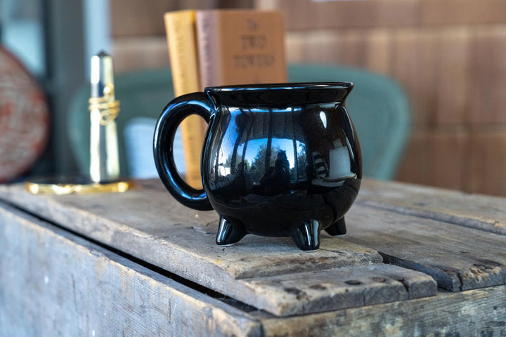 Black glossy cauldron-style coffee mug with side handle, on wooden surface.