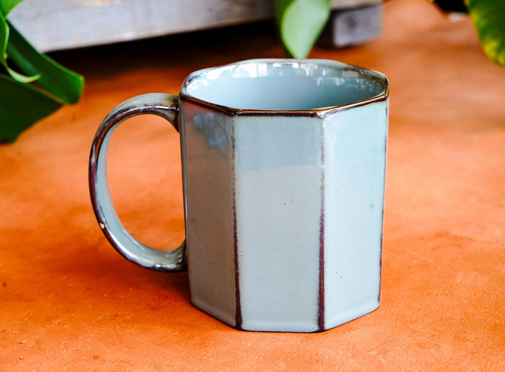 Light blue octagonal ceramic mug with side handle, glossy glaze and dark trim