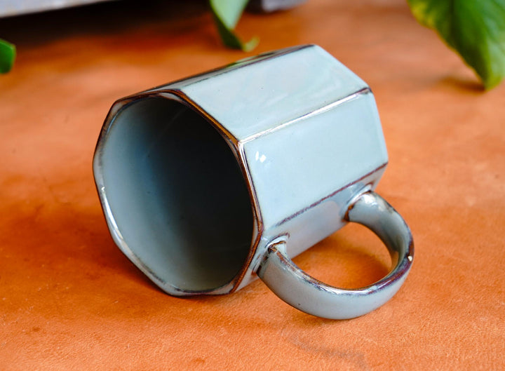 Octagonal ceramic mug with curved handle, glossy dark interior and light blue exterior