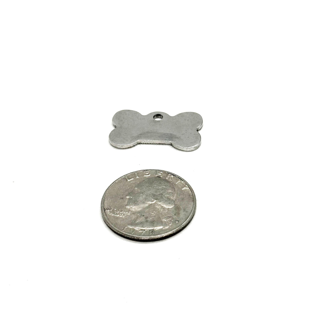 Silver bone-shaped charm with small hole, shown with metal coin for scale.