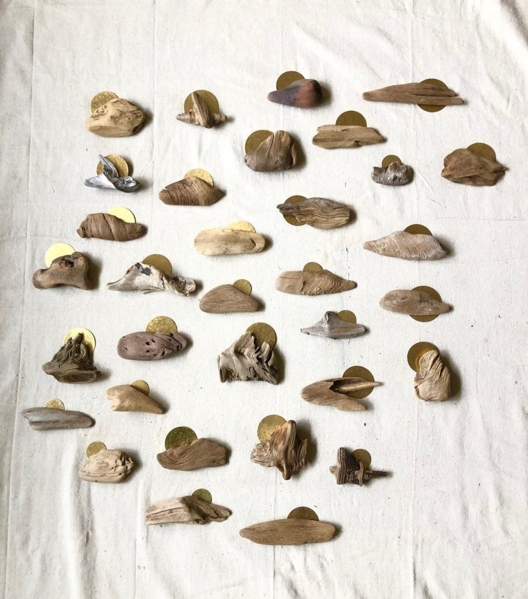 Driftwood wall sculpture assortment of small carved pieces on light fabric with gold disks