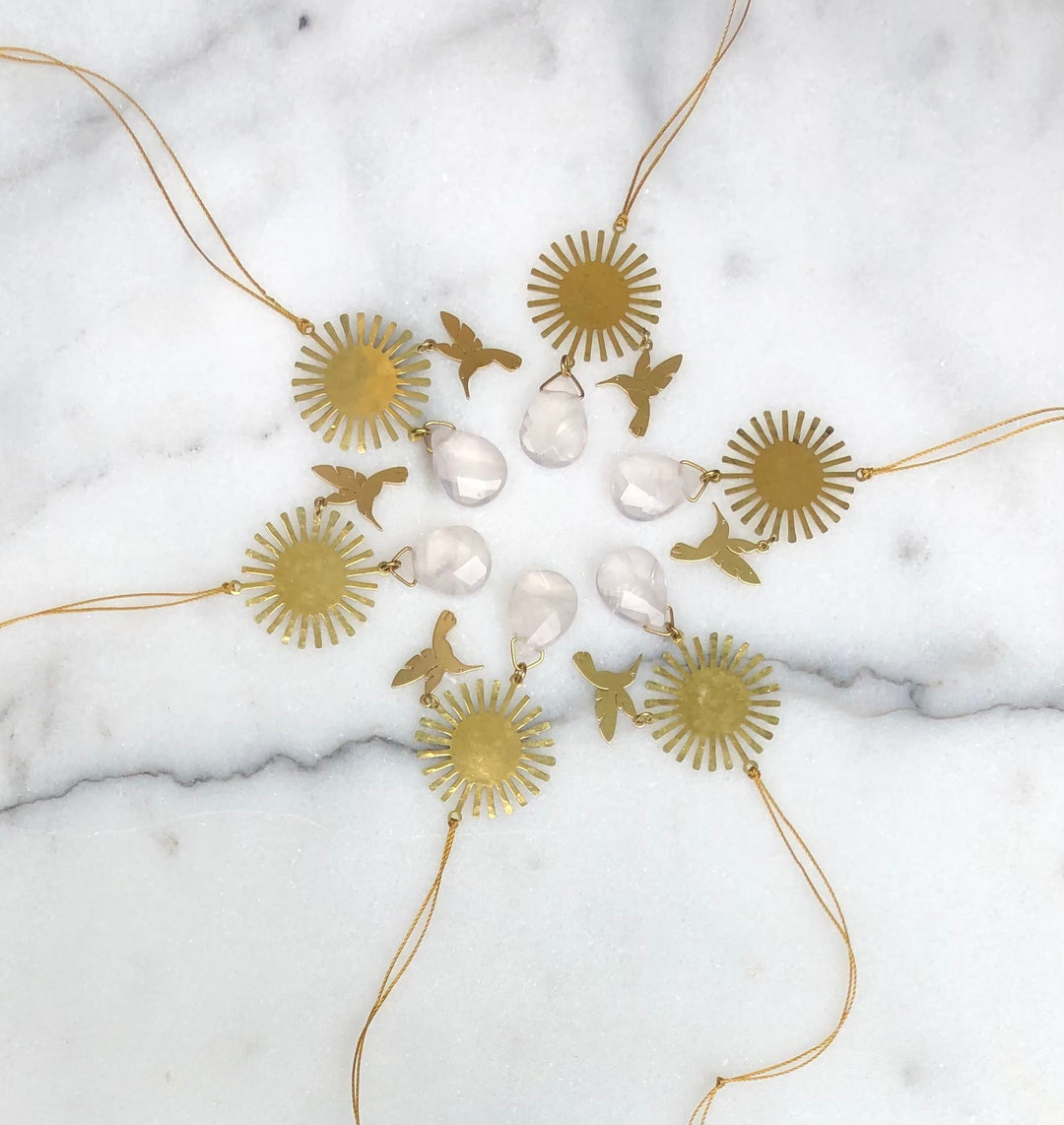 Gold-tone rose quartz ornament set with sunburst charms, bird cutouts, and hanging cords
