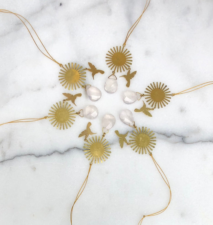 Gold-tone rose quartz ornament set with sunburst charms, bird cutouts, and hanging cords