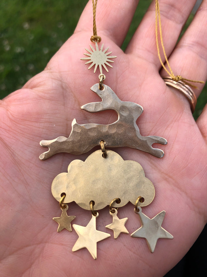 Metal holiday ornament in hand: sunburst charm, gold cloud, and dangling star pieces