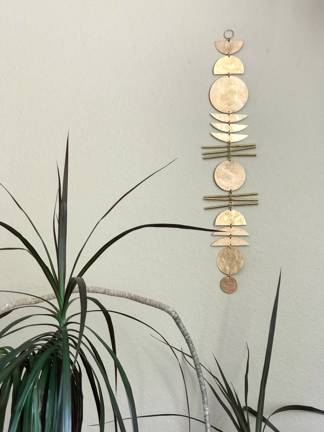 Gold-tone disk wall hanging with small scalloped charms, hanging on a pale wall