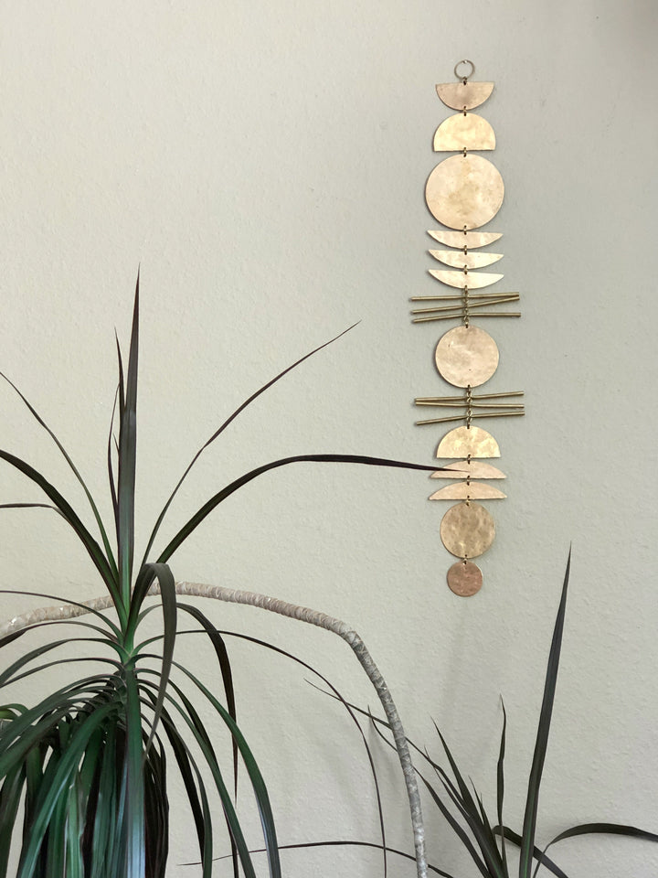 Gold-tone disk wall hanging with small scalloped charms, hanging on a pale wall