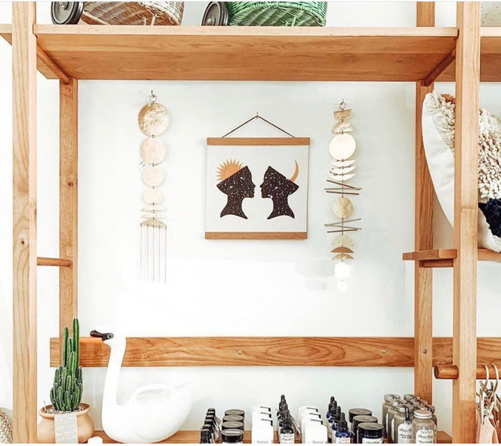 Gold-tone disk wall hanging with dangling rings on a wooden display frame
