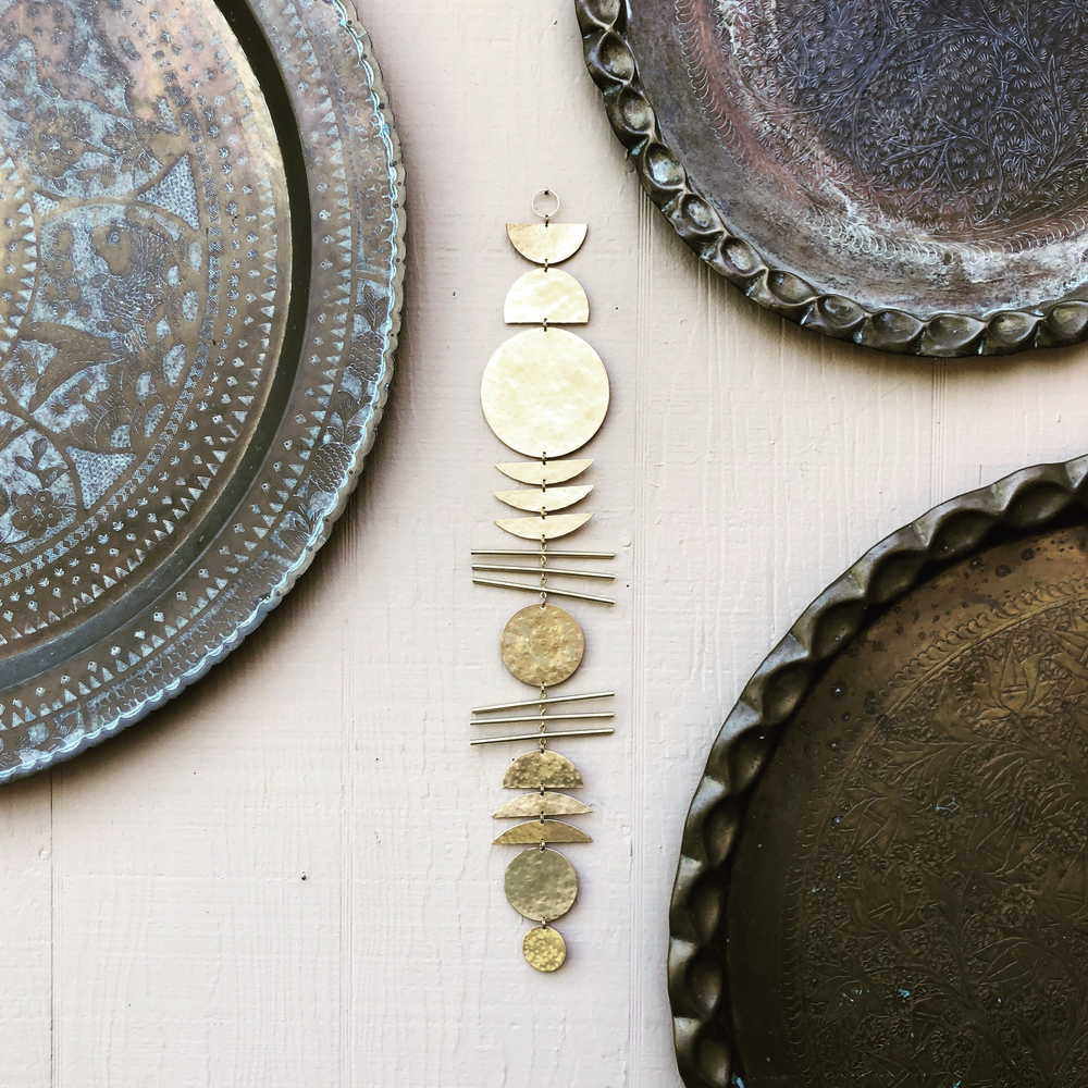 Gold-tone stacked metal disk wall decor with thin bar accents on a white wall