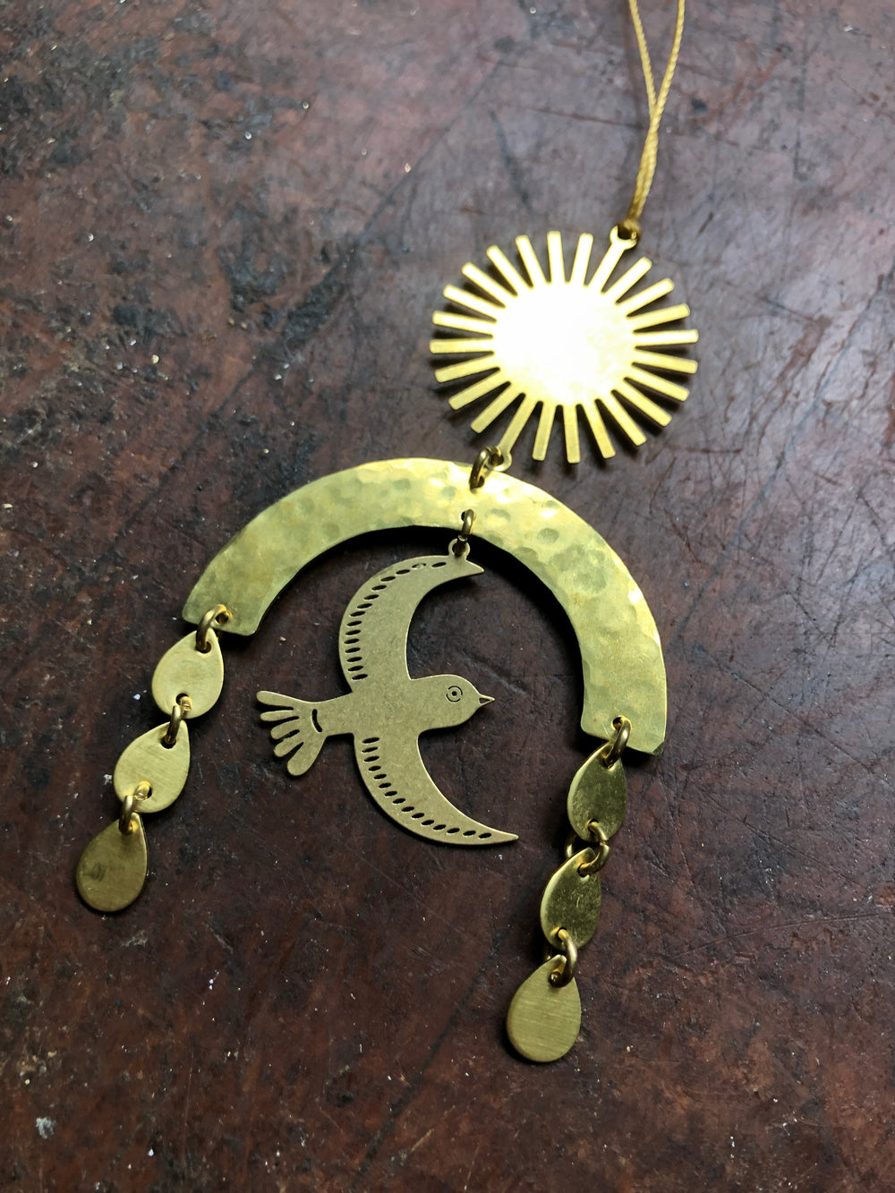 Gold crescent ornament with bird silhouette, sun disc top, and four dangling leaf charms