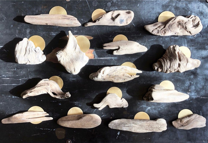 Collection of driftwood sculptures with gold circular metal backing on a dark panel