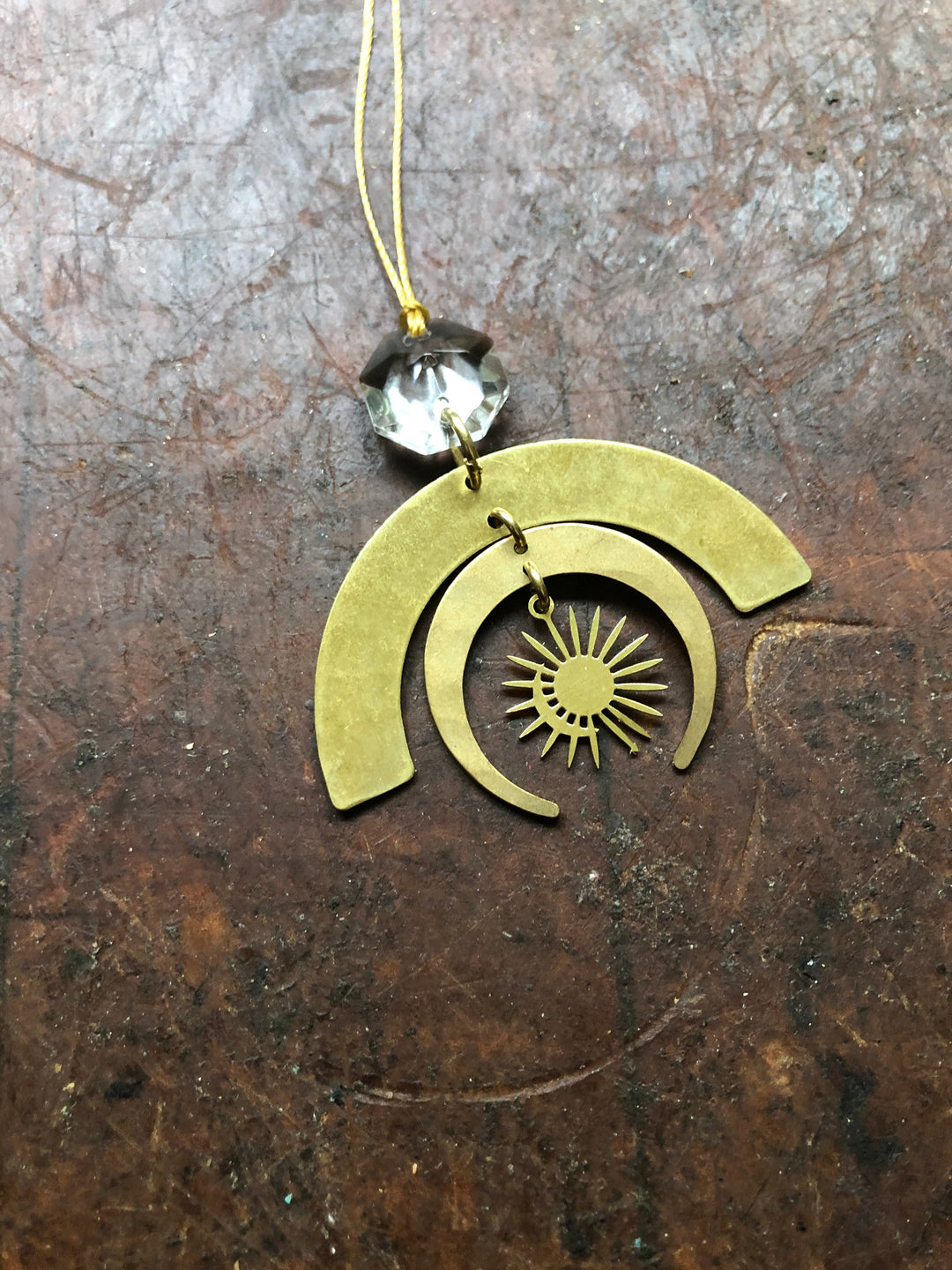 Gold-tone crescent ornament with clear glass crystal drop and engraved sunburst motif.