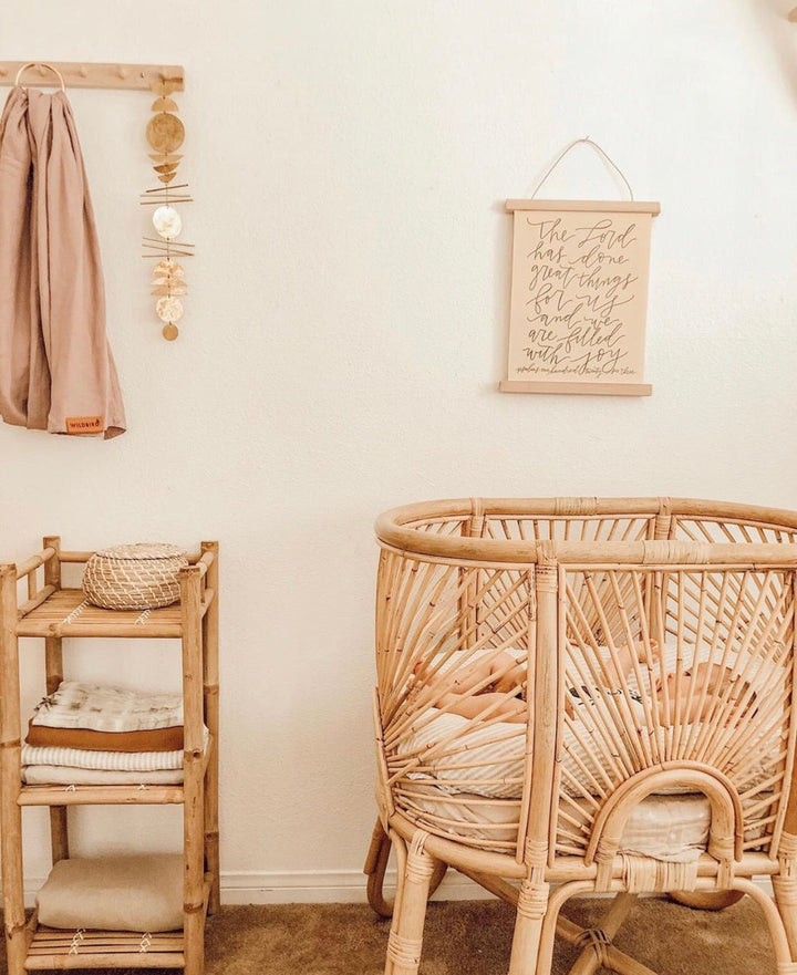 Gold-tone disk wall hanging on a light wall near a rattan chair and shelf decor