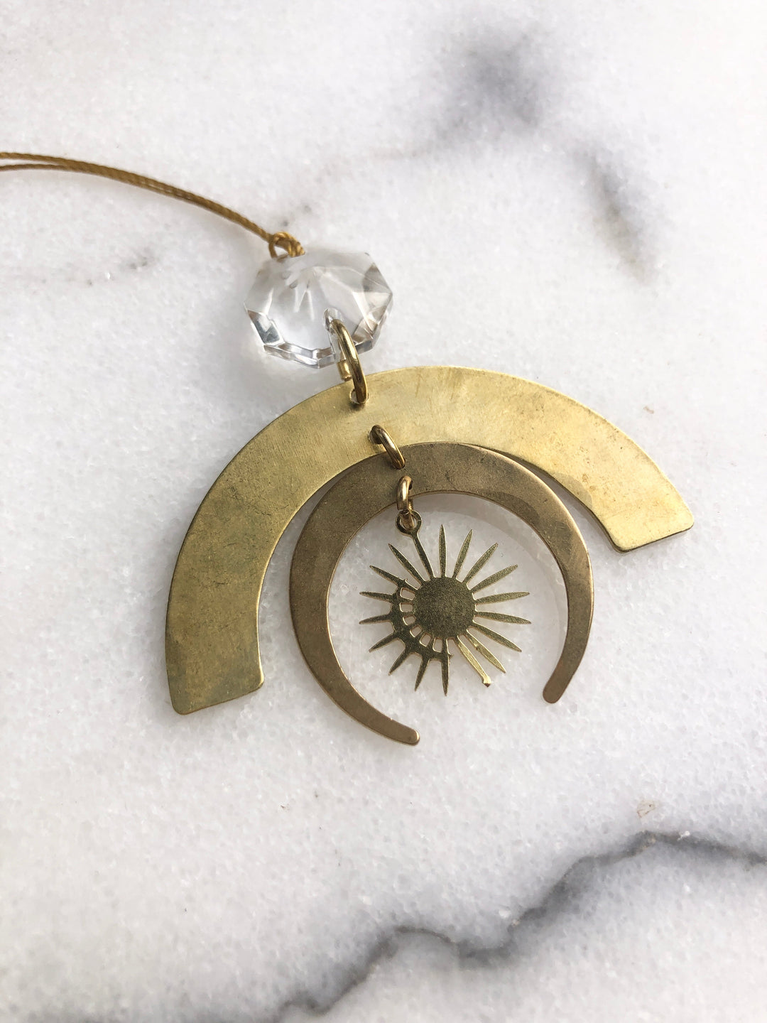 Gold-tone crescent ornament with clear glass crystal and sunburst design on inner ring.