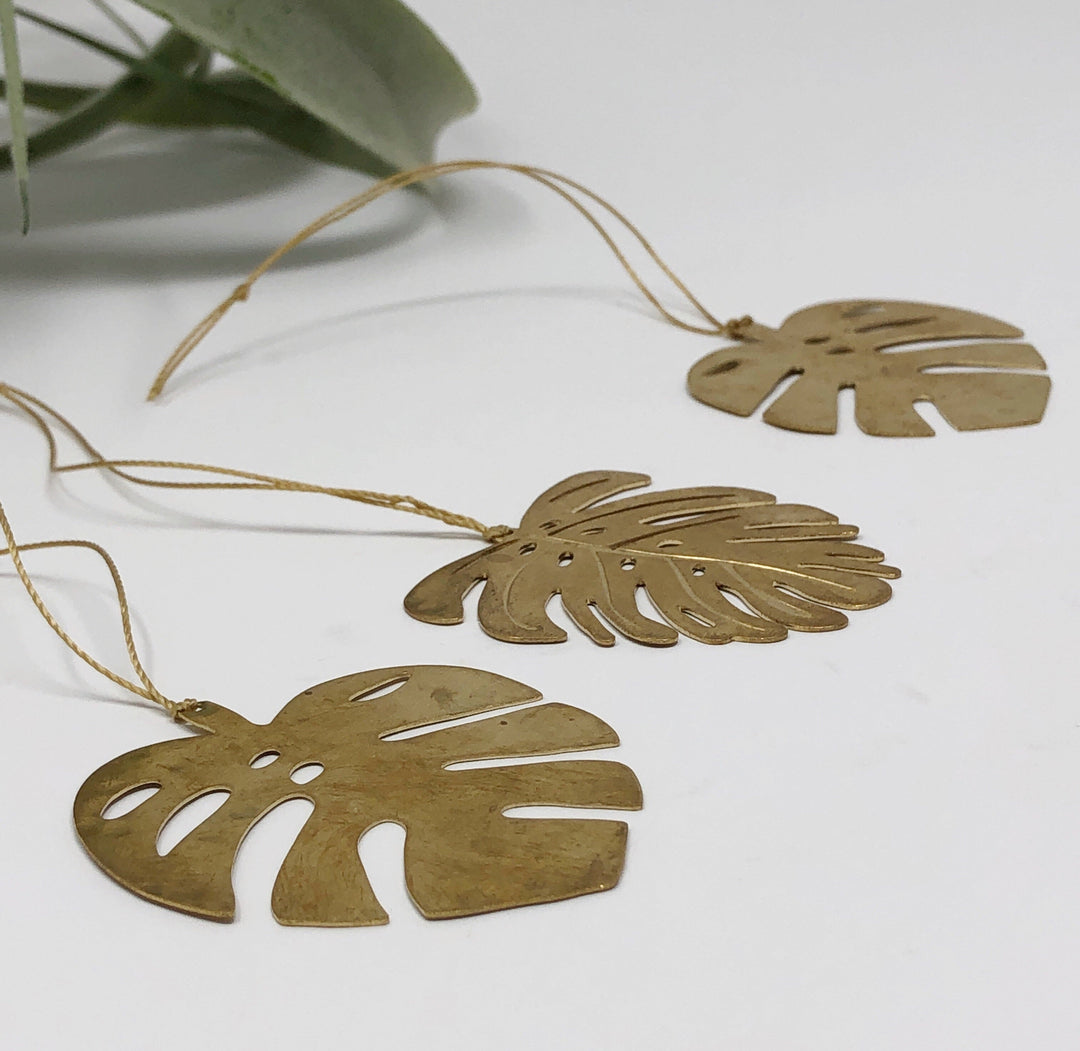 Close-up of gold monstera leaf ornaments with cutout details on thin cords