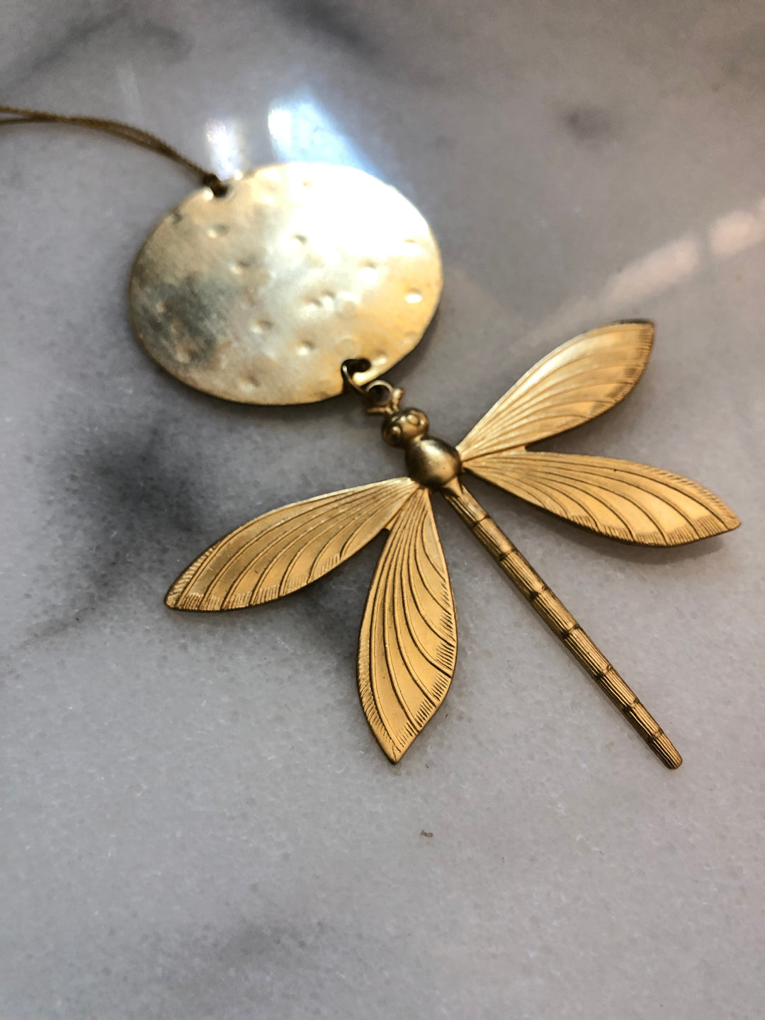 Gold-tone dragonfly ornament, round top disc with hanging cord and four layered wings.