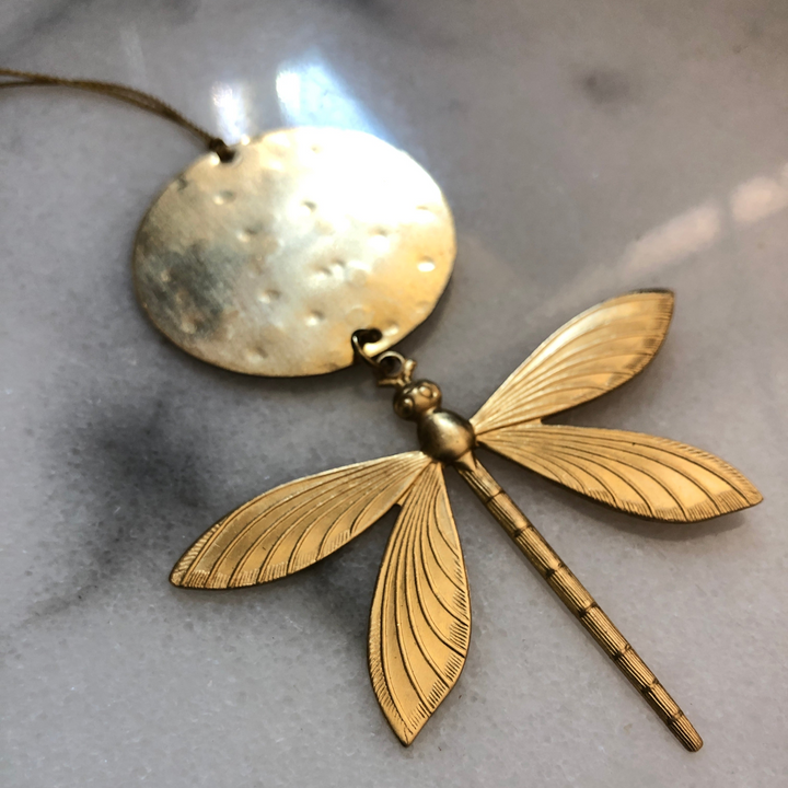 Gold-tone dragonfly ornament with round tag and textured wings, hanging on a loop.