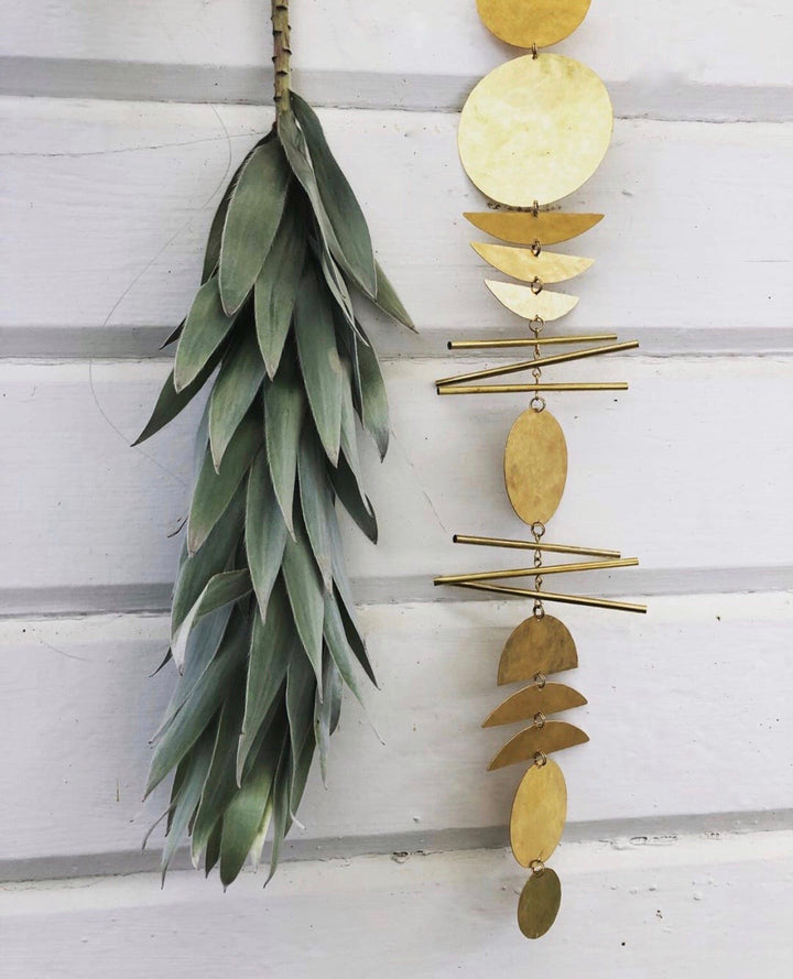 Gold-tone disk wall hanging with thin bars, shown beside long green feather bundle