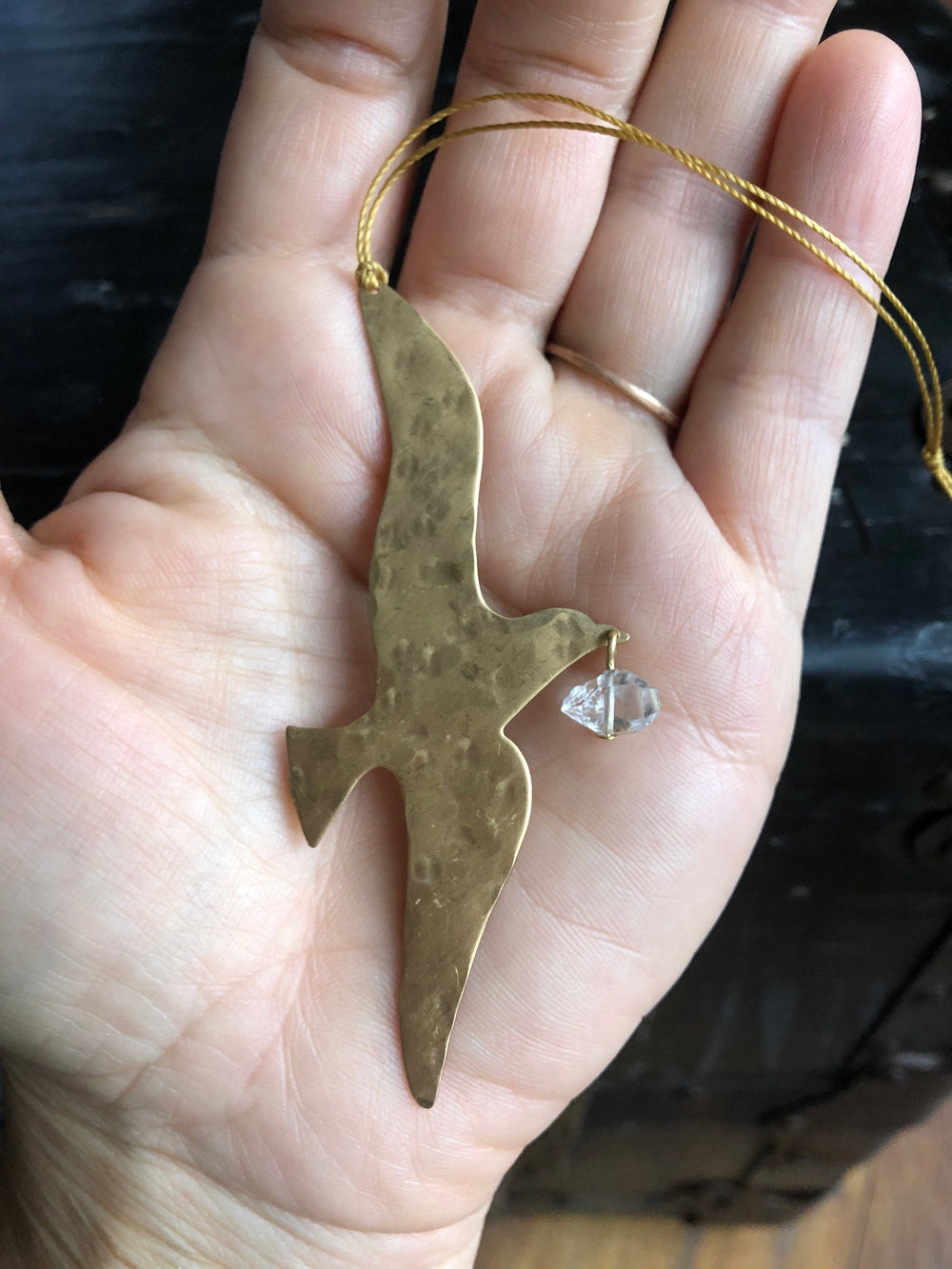 Gold-toned hammered ornament with clear Herkimer diamond on cord, in hand