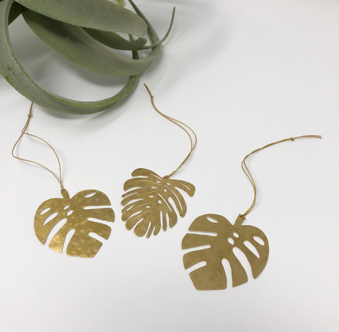 Gold leaf ornament set with three monstera-shaped cutouts on string cords