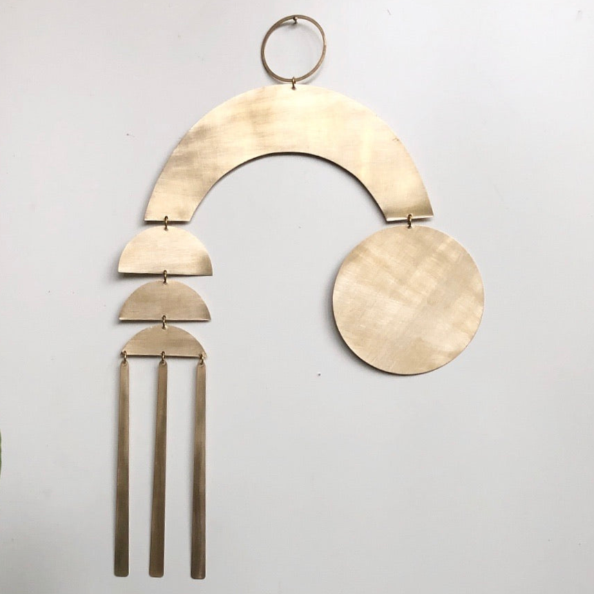 Beige wood arc wall hanging with round disc and three tassels on a metal ring.