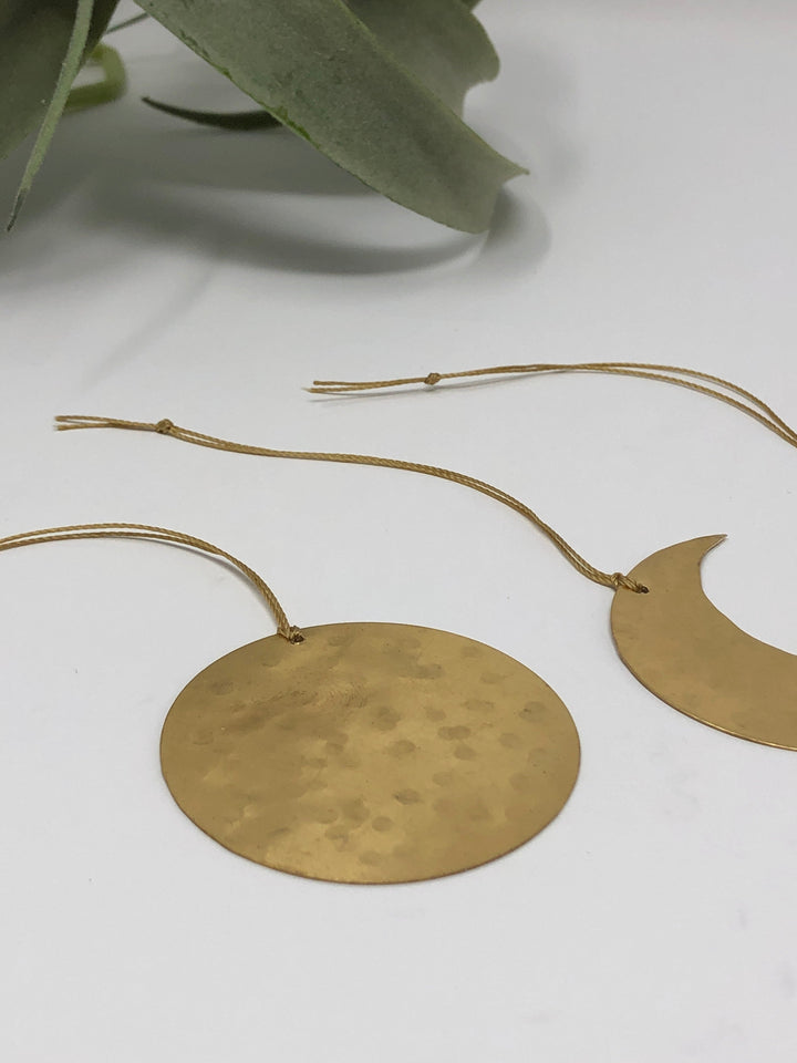 Gold round disk and crescent moon ornaments on hanging cords with leafy accents