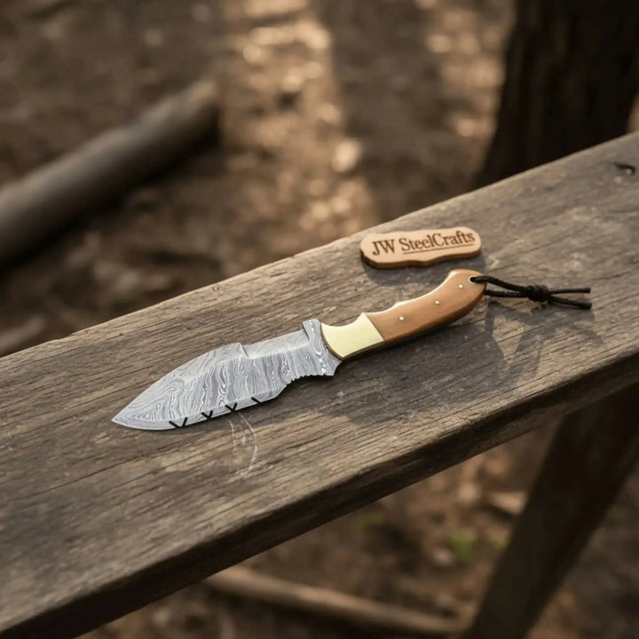 Damascus steel survival knife with tan handle and patterned blade on wood