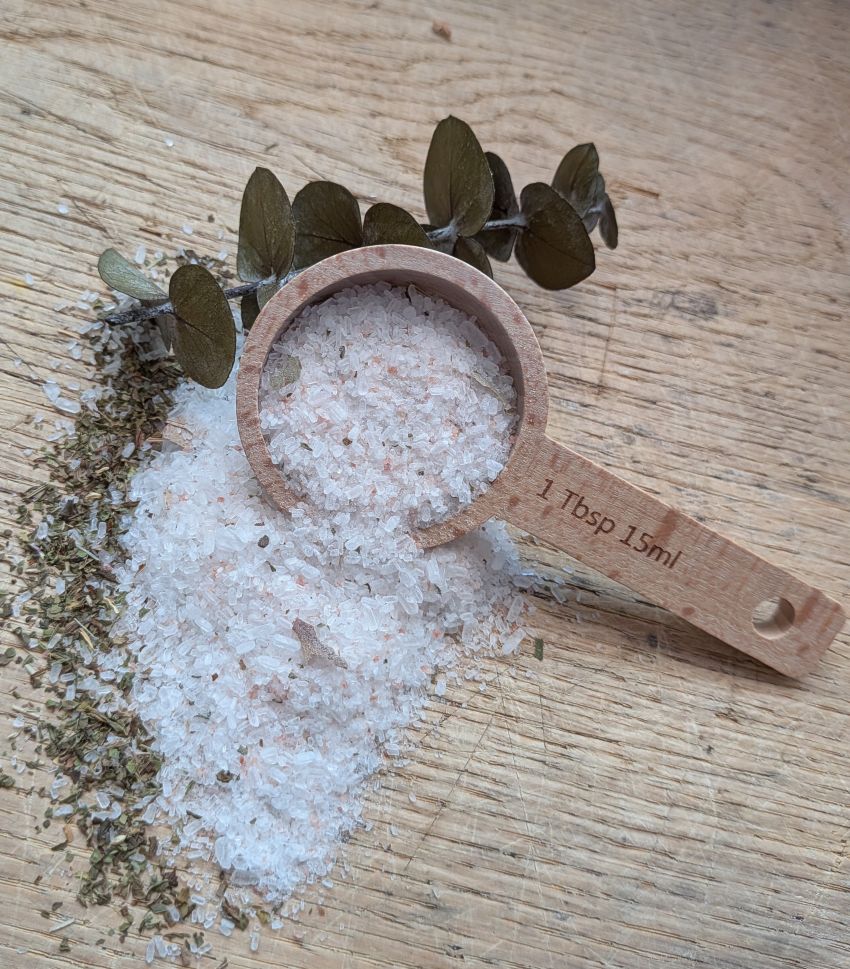 Bath salt crystals in wooden scoop with dried leaves and measuring spoon