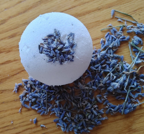 Round lavender bath bomb with dried lavender flower pieces on top, pale blue-purple