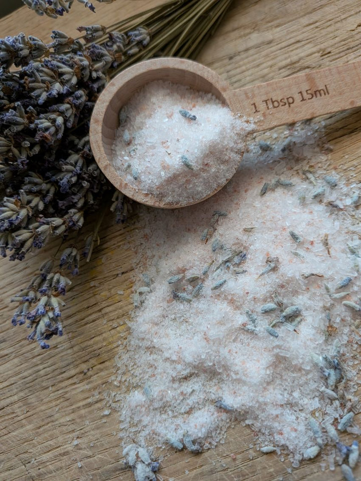 Bath salt crystals with lavender sprigs around wooden scoop and 1 tbsp measure