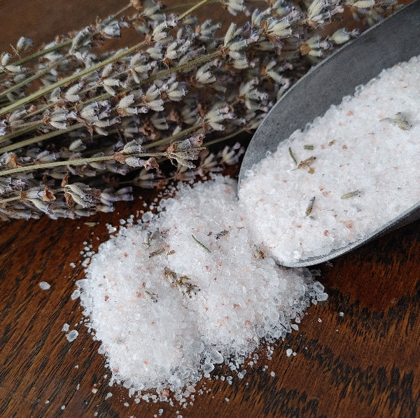 Scoop of bath salt crystals with dried lavender buds and stems on wood