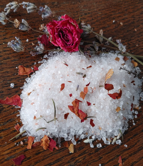 Rose-scented bath salt crystals with dried rose petals scattered on wood
