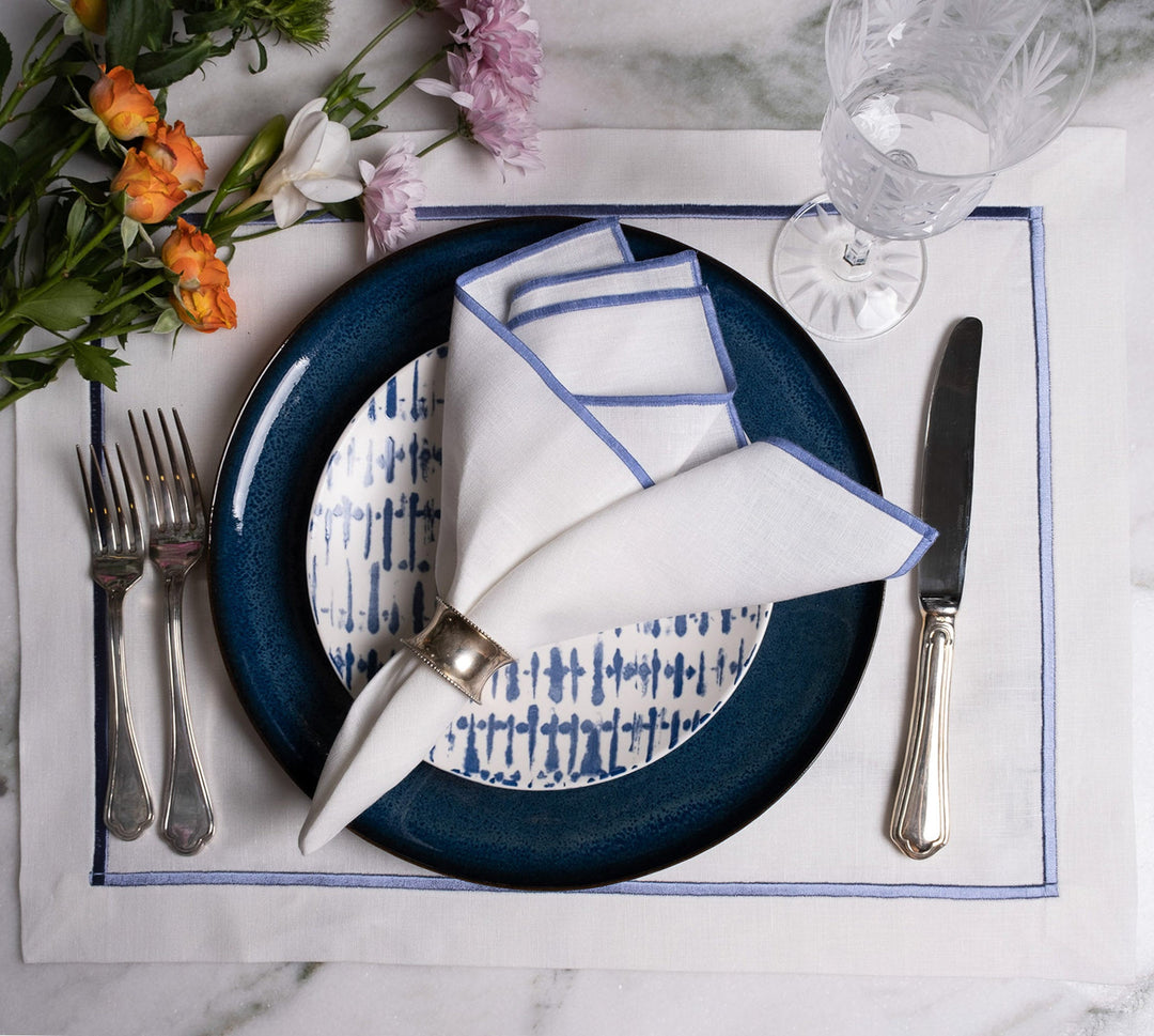 Linen napkins on a place setting, white fabric with blue stitched border, folded