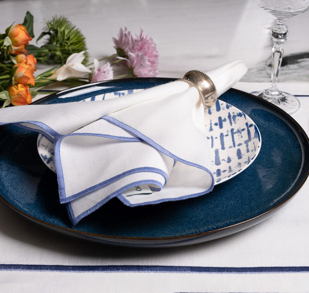 Linen napkins on a plate, white with blue stitched edge, neatly folded