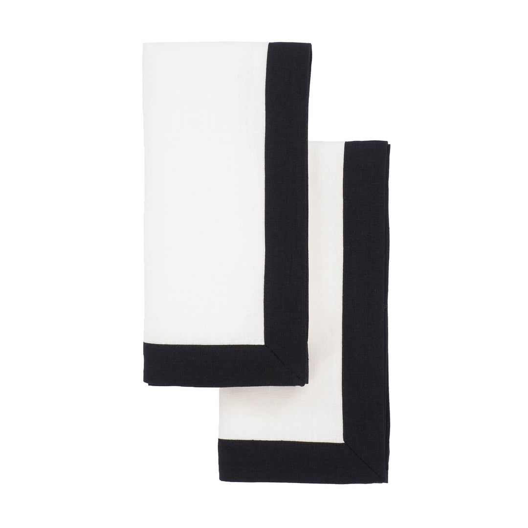 Two folded linen napkins overlapping, white fabric with black border trim.
