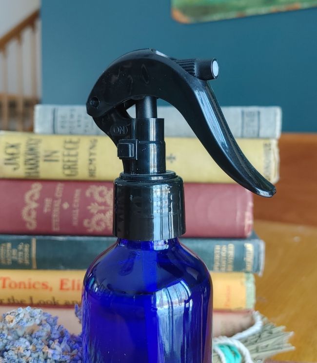 Deodorizing bathroom spray bottle in blue glass with black trigger sprayer head.