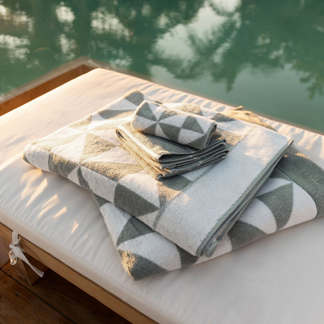 Folded sage and ecru cotton towels with geometric blocks on a bed