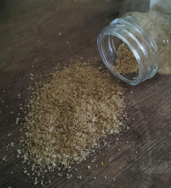 Brown bath soak granules spilled beside open glass jar on wooden surface