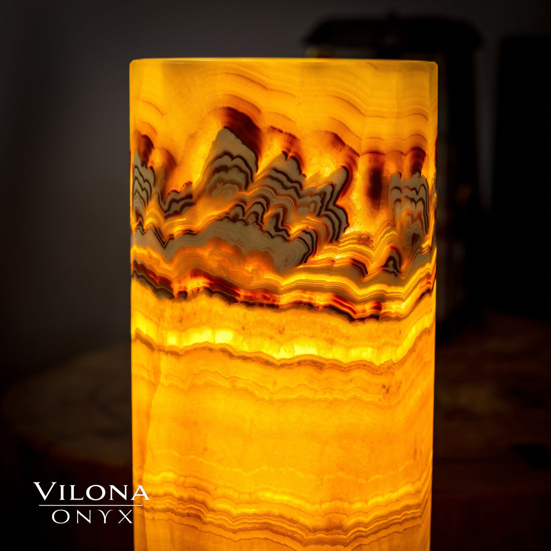 Onyx cylinder table lamp close-up, bright amber glow through carved stone