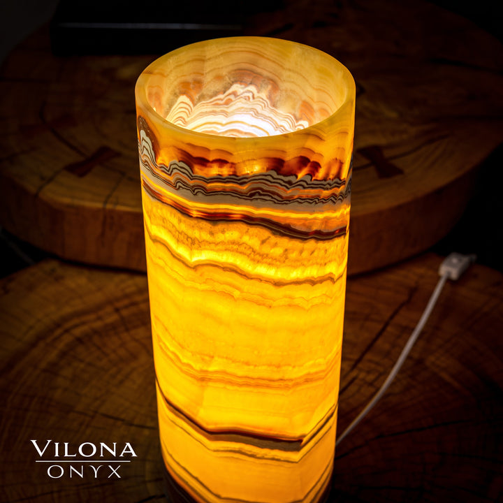 Onyx cylinder table lamp showing lit circular top opening and amber striped pattern