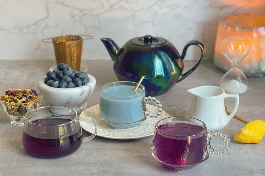 Teapot and cups filled with purple berry tea with blueberries on the side