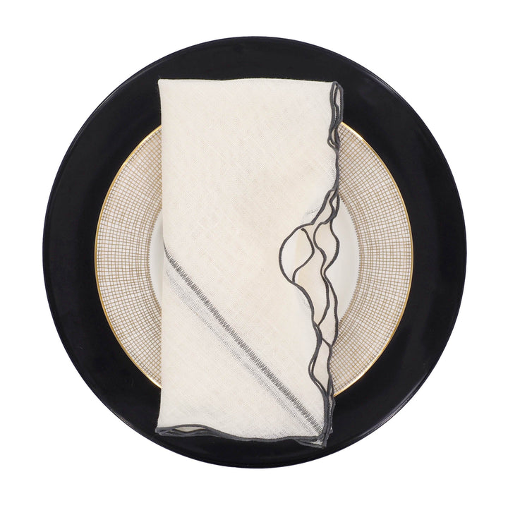 Off-white linen napkin with charcoal ruffled edge placed on a plate