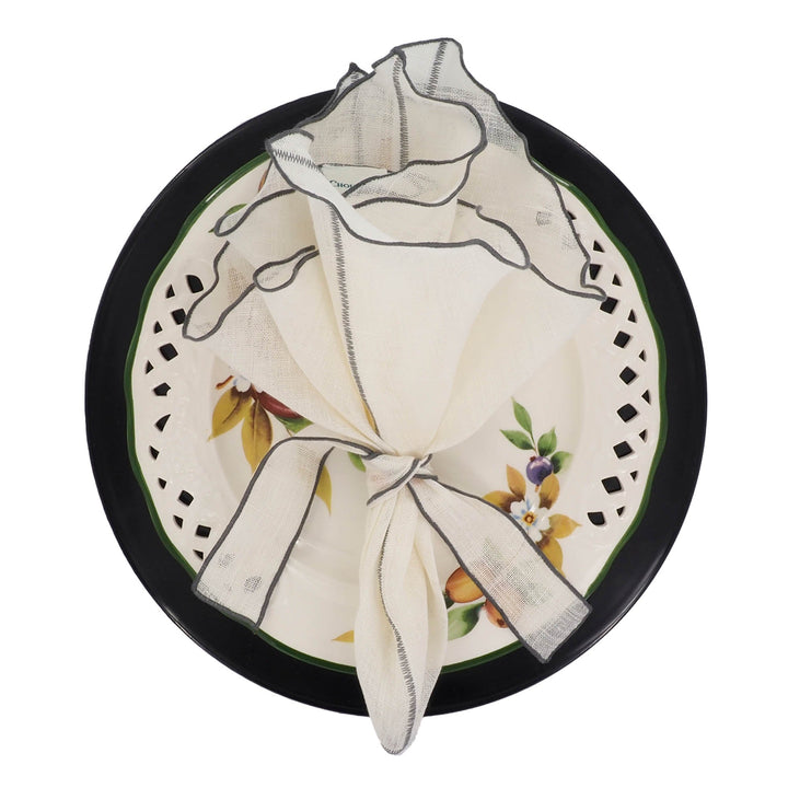 Off-white linen napkin with charcoal ruffled edge and stitched border, folded on plate