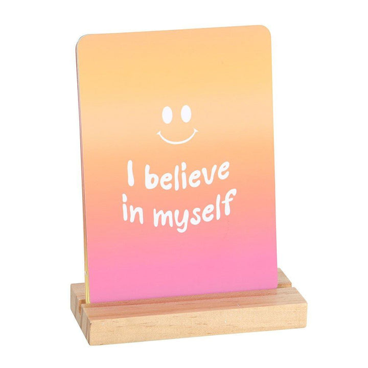 Affirmation card on wooden stand, orange-magenta gradient: "I believe in myself"
