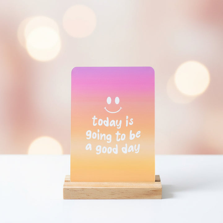 Affirmation card on wooden stand, purple-orange gradient: "today is going to be a good day"