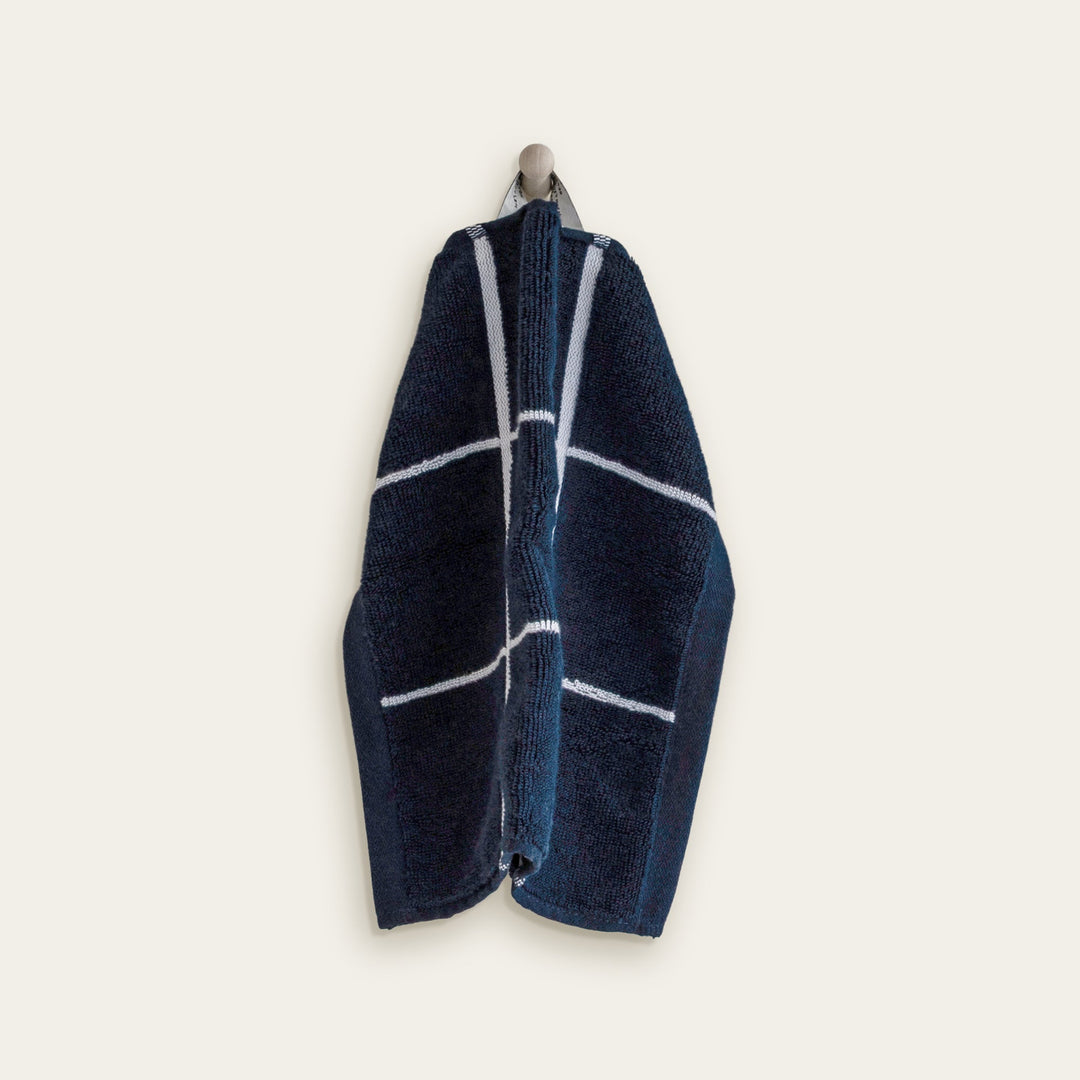Navy and white cotton towel with intersecting white stripe lines, folded and hanging.