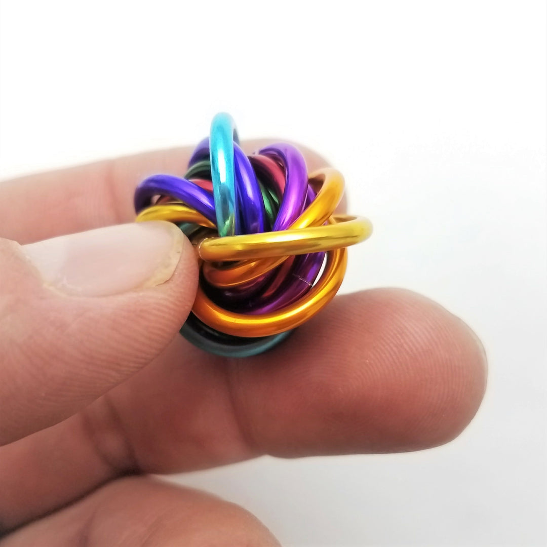 Shiny multicolor fidget stress ball held between fingers; glossy rainbow interlocked rings.