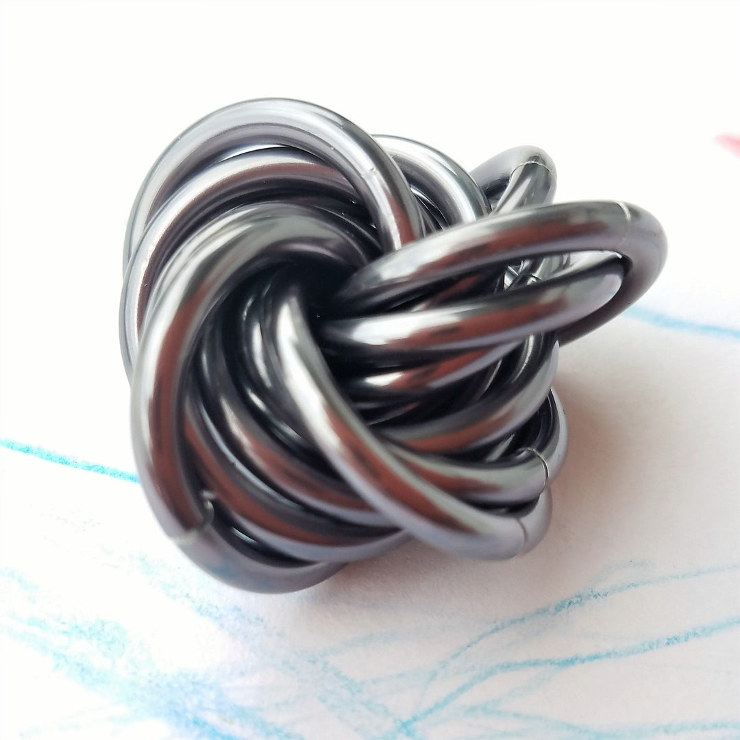 Swirled fidget stress ball, dark metallic loops with reflective silver highlights